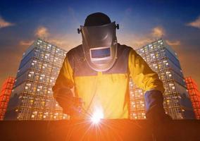 Industrial welding worker with safety equipments and protective mask welding steel structure with cargo container stack in background for transportation import,export and logistic industrial concept photo