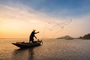 Asian fisherman with his wooden boat in nature river at the early morning before sunrise photo