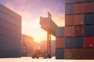 Forklift truck lifting cargo container in shipping yard or dock yard against sunrise sky with cargo container stack in background for transportation import,export and logistic industrial concept photo