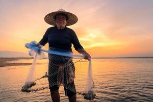Silueta de pescador asiático sostenga una red para pescar peces de agua dulce en el río natural temprano en la mañana antes del amanecer