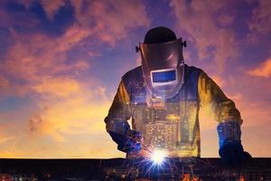 Double exposure of a downtown city and Industrial Worker welding steel structure with sunset sky in background for industrial and construction concept