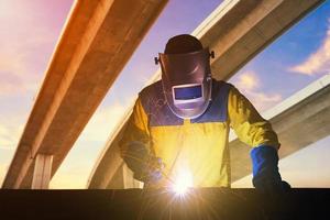 Industrial Worker with safety equipments and protective mask welding steel structure with expressway the infrastructure for transportation in background. Elegant design for construction concept photo