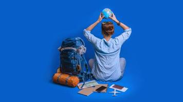 vacaciones de planificación turística con la ayuda del mapa del mundo con otros accesorios de viaje alrededor. viajero mujer con maleta sobre fondo de color azul. chica con una bola de globo en la mano. mochila de viaje foto