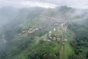 Aerial view of foggy mountain and hut resort on hillside in tropical rainforest on rainy day photo