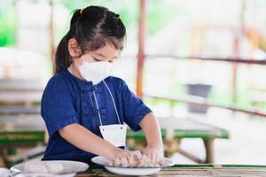 Girl mixing white clay with salt and water to create viscous consistency. Child in food preservation class. Little farmer. Kid wear face mask to prevent spread of respiratory virus. photo