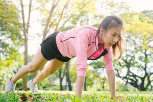 Asian young woman warm up her body by push up to build up her strength before morning jogging exercise and yoga on the grass under the warm light sunshine in the morning. Exercise outdoor concept. photo