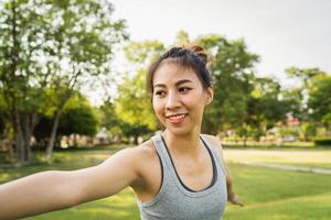 Mujer joven sana asiática del corredor que calienta el cuerpo que se estira antes del ejercicio y del yoga cerca del lago en el parque bajo la luz cálida de la mañana. estilo de vida fitness y mujeres activas se ejercitan en el concepto de ciudad urbana. foto