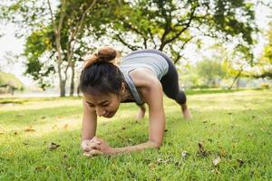 Joven y saludable corredor asiático calienta su cuerpo empujando hacia arriba antes de hacer ejercicio y hacer yoga cerca del lago en el parque bajo la cálida luz de la mañana. estilo de vida fitness y mujeres activas se ejercitan en el concepto de ciudad urbana. foto