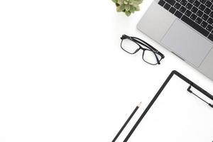 Creative flat lay photo of workspace desk. Top view office desk with laptop, glasses, pencil, blank clipboard and plant on white color background. Top view with copy space, flat lay photography.