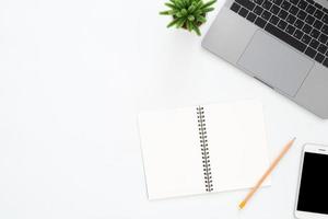 Creative flat lay photo of workspace desk. Top view office desk with laptop, phone, pencil, notebook and plant on white color background. Top view with copy space, flat lay photography.