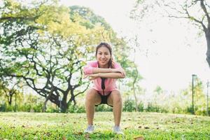 Young asian woman do squats for exercise to build up her beauty body in park environ with green trees and warm sunlight in the afternoon. Young woman workout exercise at the park. Outdoor exercising.