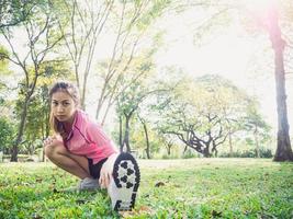 mujer asiática joven sana que ejercita en el parque. Colocar joven haciendo entrenamiento de entrenamiento en la mañana. joven mujer asiática feliz que se extiende en el parque después de un entrenamiento corriente. ejercicio concepto al aire libre. foto