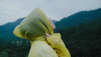 Young Asian woman feeling happy playing rain while wearing raincoat walking near forest. Lifestyle women enjoy and relax in rainy day. photo