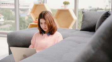 Young asian woman doing research work for her business. Smiling woman sitting on sofa relaxing while browsing online shopping website. Happy girl browsing through internet during free time at home. photo