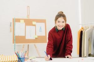 Hermosa diseñadora de moda asiática profesional que trabaja con bocetos de tela y diseño de ropa de dibujo en el estudio. concepto de trabajo de las mujeres de estilo de vida. foto