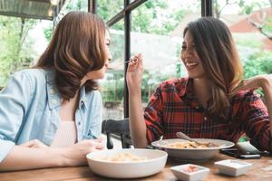 Beautiful happy Asian women lesbian lgbt couple sitting each side eating a plate of Italian seafood spaghetti and french fries at restaurant or cafe while smiling and looking at food. photo