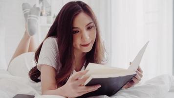 Portrait of beautiful attractive Asian woman reading a book while lying on the bed when relax in her bedroom at home. Lifestyle women using relax time at home concept.
