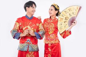 año nuevo chino, el hombre y la mujer visten cheongsam sonriendo para dar la bienvenida a lo bueno con dinero de regalo y abanico de mano