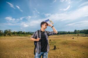 A male traveler with a backpack carrying a map and standing on the meadow. photo