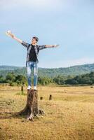 A male traveler with a backpack, carrying a map and standing on a tree stump photo