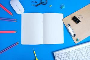 On top of the office desk table with laptop computer and supplies is a small blank notebook with pen. Flat lay, top view with copy space. photo