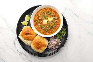 Indian Mumbai Street style Pav Bhaji, garnished with peas, raw onions, coriander, and Butter. Spicy thick curry made of out mixed vegetables served with pav over white background with copy space. photo