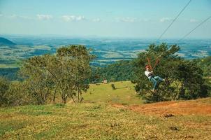 Pardinho, Brazil - May 31, 2018. Woman descending by cables in a sport called zip-line over meadows and trees in a valley near Pardinho. A small rural village in the countryside of Sao Paulo State. photo