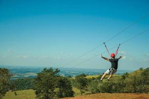 Pardinho, Brazil - May 31, 2018. Man descending by cables in a sport called zip-line over meadows and trees in a valley near Pardinho. A small rural village in the countryside of Sao Paulo State. photo