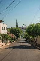 sao manuel, brasil, 14 de octubre de 2017. vista de la calle cuesta abajo con árboles en la acera, paredes y casas en un día soleado en sao manuel. un lindo pueblito en el campo del estado de sao paulo. foto