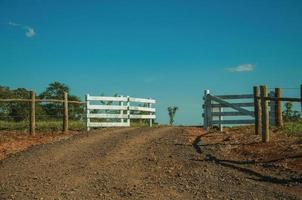 Pardinho, Brazil - May 31, 2018. Wooden farm gate and cattle guard in the middle of barbed wire fence, in a sunny day near Pardinho. A small rural village in the countryside of Sao Paulo State. photo