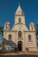 fachada de la iglesia y campanario frente a una pequeña plaza de adoquines con jardín siempre verde, en un día soleado en sao manuel. un lindo pueblito en el campo del estado de sao paulo. sudeste de brasil. foto