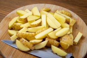 patatas crudas cortadas en patatas fritas sobre una tabla de madera.