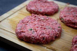 carne cruda preparada para hamburguesas. carne sazonada en una tabla de madera. foto