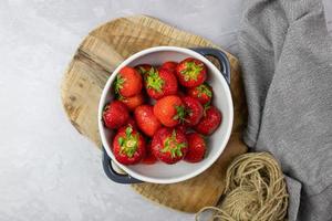 Fresh strawberries in a bowl lying on a wooden board. Delicious seasonal fruit. Top view. photo