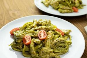 Pasta with pieces of chicken, basil pesto, and tomatoes. Delicious dinner. photo