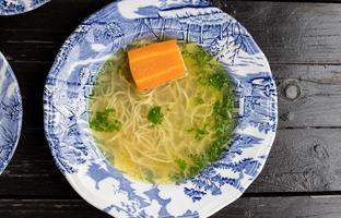 Broth with noodles and carrots in a decorative plate. View from above. photo