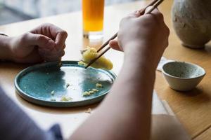 una persona comiendo sushi en un restaurante. manos visibles sosteniendo palillos. foto