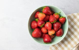 Fresh strawberries in a mint bowl on a white table from above