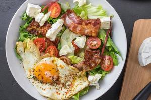 Perfect salad during a ketogenic diet. Full of fats. Fried egg, tomatoes, bacon, lettuce, and cheese. View from above. photo