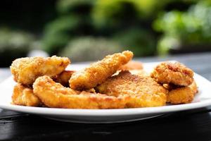 Breaded chicken pieces on a plate in a garden background.