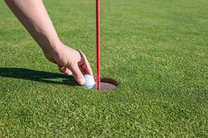 A person pulling a golf ball out of a hole on a golf course golf concept photo