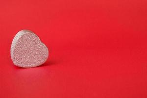 Silver gift box in the form of a heart on a red background. Closeup copy space photo