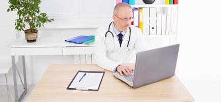 doctor works at a laptop at his desk in clinic photo