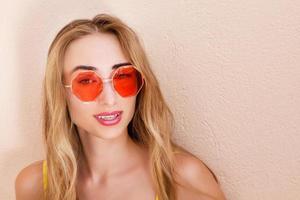 Fashion portrait pretty woman in summer red sunglasses over colorful peach background photo