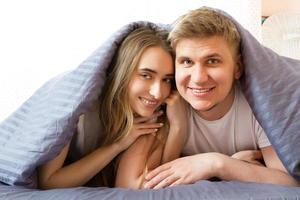 Happy smiling teen couple under blanket on bed in the morning - love relationship concept photo