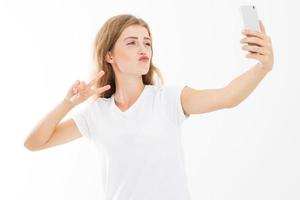 bonita chica hipster en camiseta blanca hace una cara de pato y toma un autorretrato con su teléfono inteligente foto