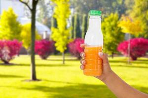 black female hand hold orange juice bottle on blurred park background, healthy lifestyle concept photo