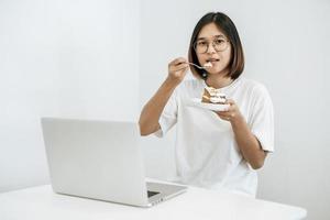 la niña come pastel y tiene una computadora portátil sobre la mesa. foto