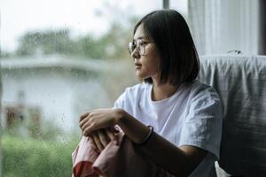 A woman in a white shirt sitting on the bed and looking out. photo