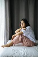 A woman in a white shirt sitting on the bed and looking out. photo